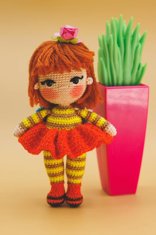 a little doll stands near a crocheted potted plant