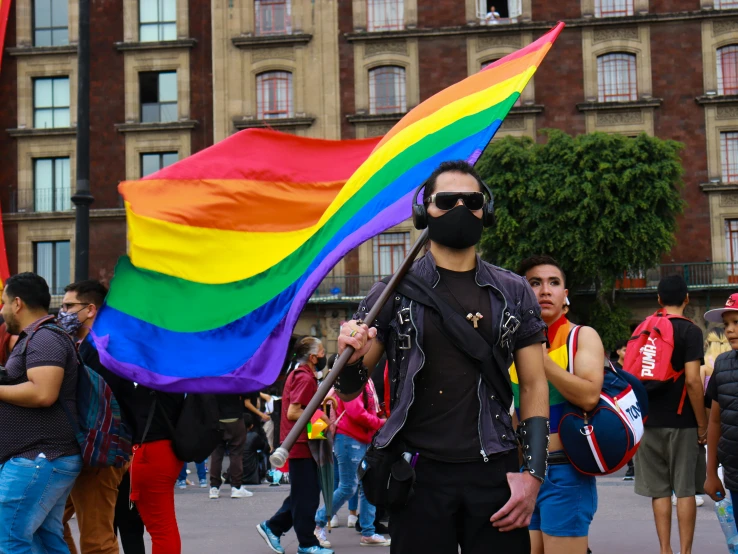 man in sunglasses holds up a rainbow flag