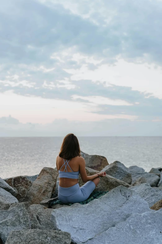 a person sits on a large rock by the ocean