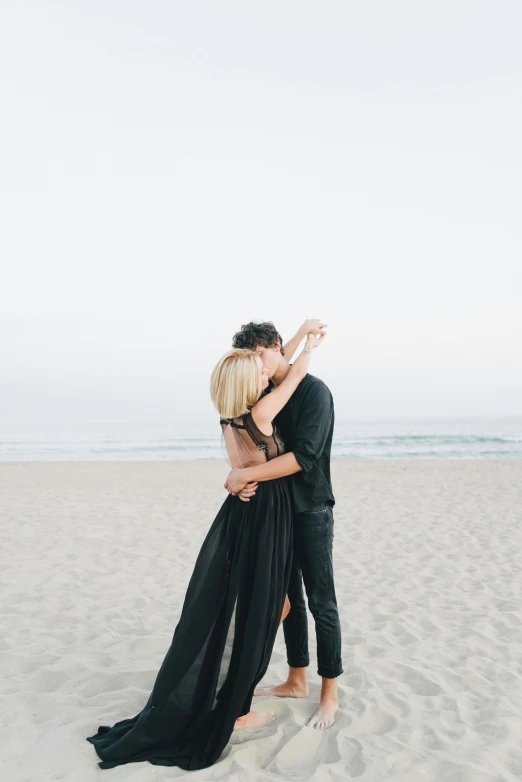 a couple hugging on the beach as they take a hug