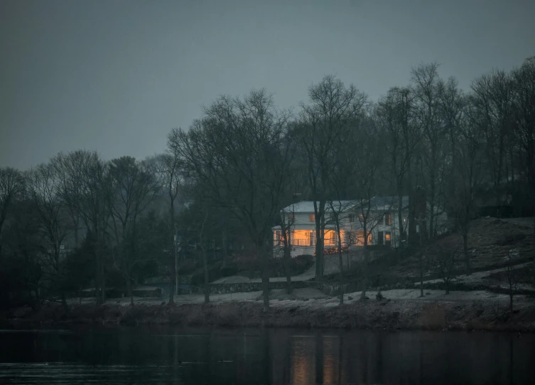 a home sits alone with its lights on across a lake