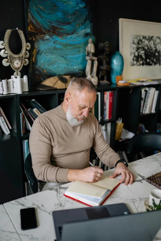 an older man is sitting at a table while he writes