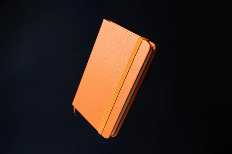 an orange book flying up against a black background