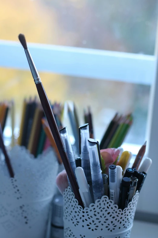 several pens, pencils and markers in a cup near a window