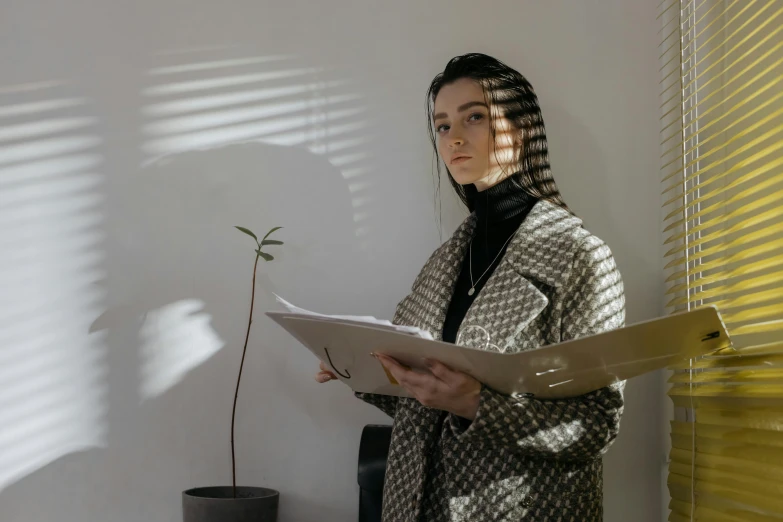 a woman stands in the shadows of blinds with a piece of paper in her hands