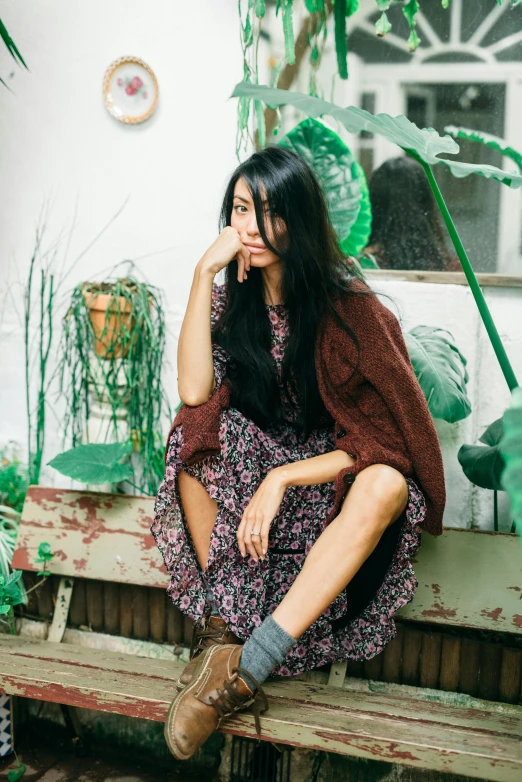 woman in long purple dress sitting on wooden bench in front of green plants