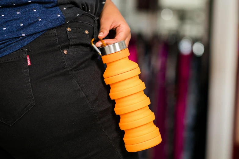 a person holding an orange water bottle on the side of their pants