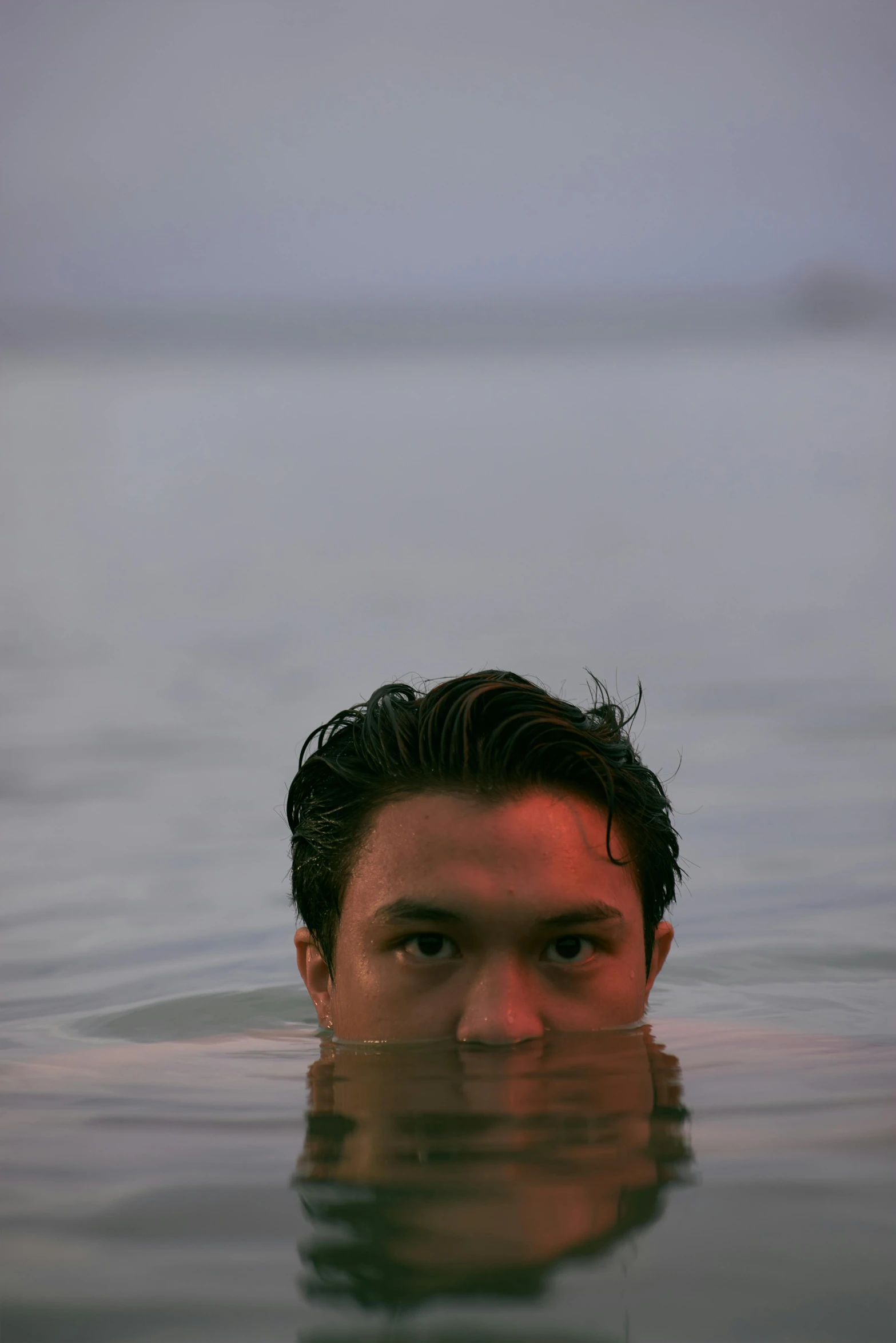 the man in the lake is in water with hair blowing back and a beard