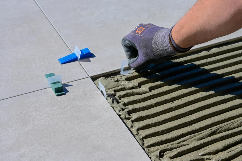 a worker in grey gloves sanding down tiles