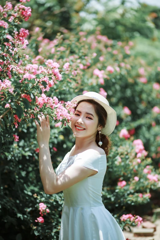 a young woman in white holds out pink flowers