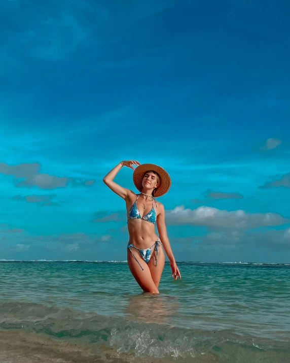 a woman in a bikini, in the water with a sun hat