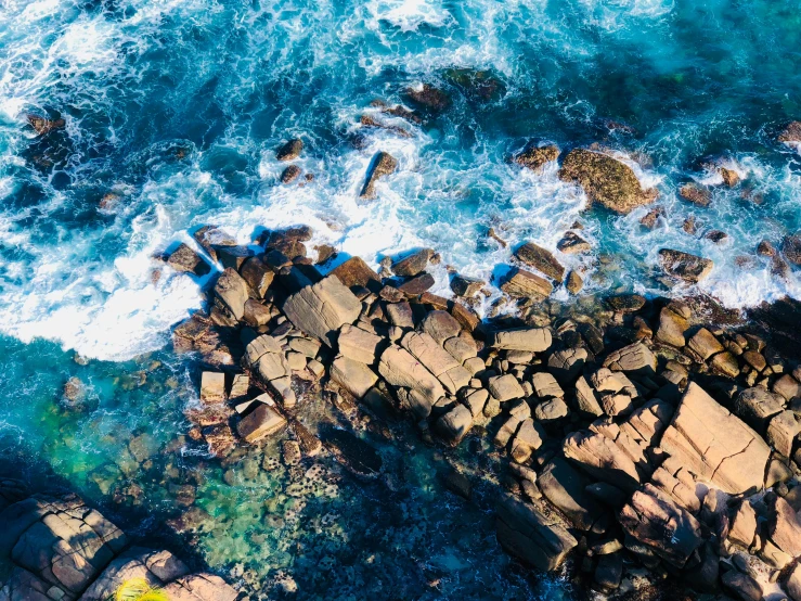 an aerial view of a rock beach with water crashing on the rocks