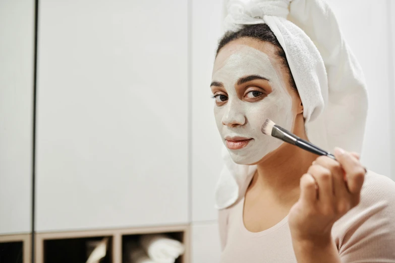 a woman with white facial mask on has a brush in her hand