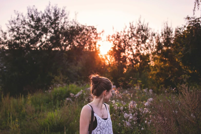 a woman walking through a field with the sun behind her