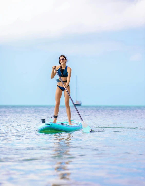 a  wearing a bikini paddling on a blue paddle boat with a sailboat in the background