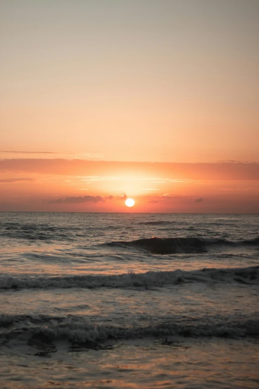 a bird flying over the ocean with the sun behind it