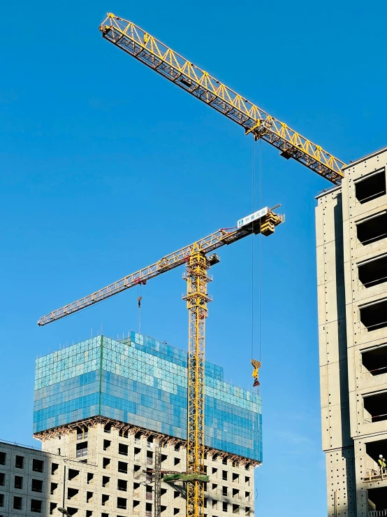 two cranes and a large building against a blue sky