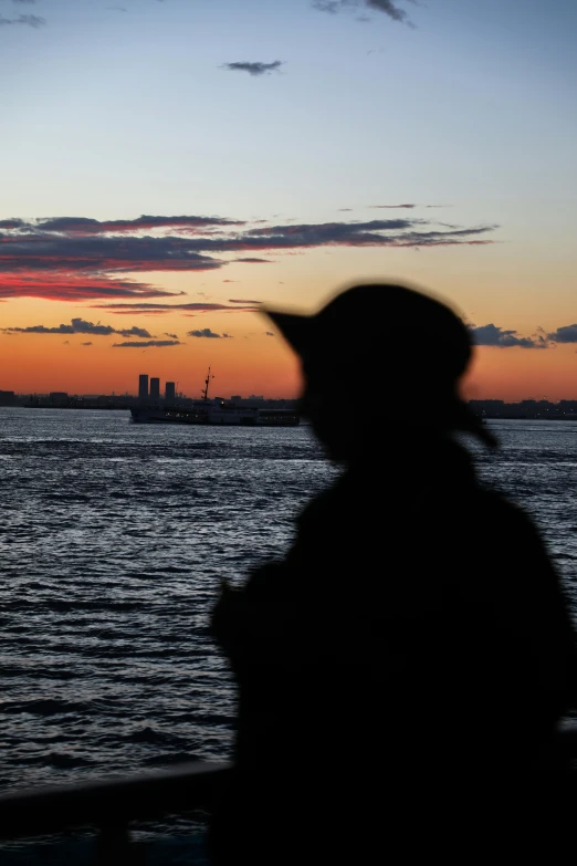 a person looking out over water with an orange and blue sky