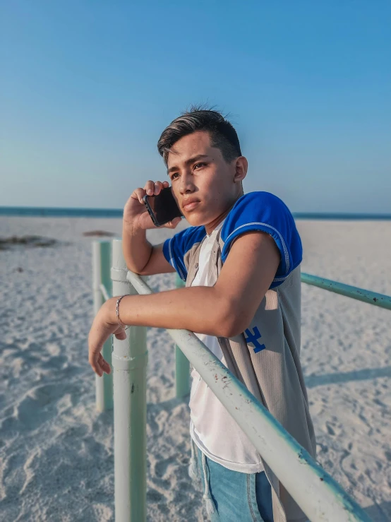 a boy leaning up against a metal pole on the beach