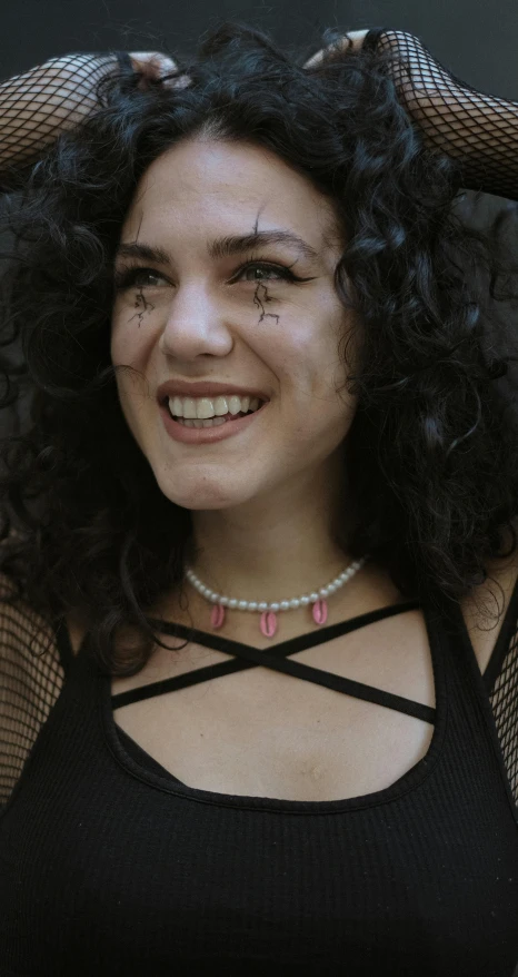 a woman has dark curly hair and a mesh black shirt on