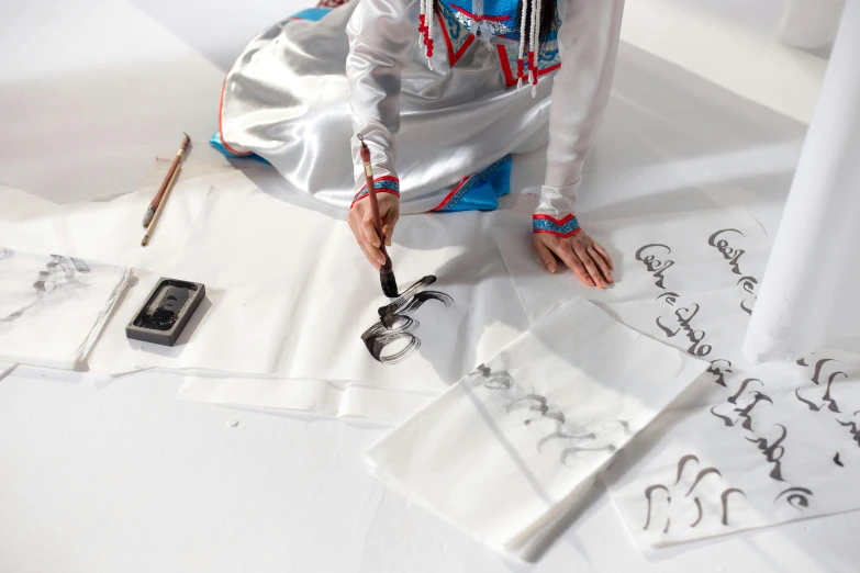 the young woman sits on the ground beside many pieces of paper and is using scissors to cut out letters