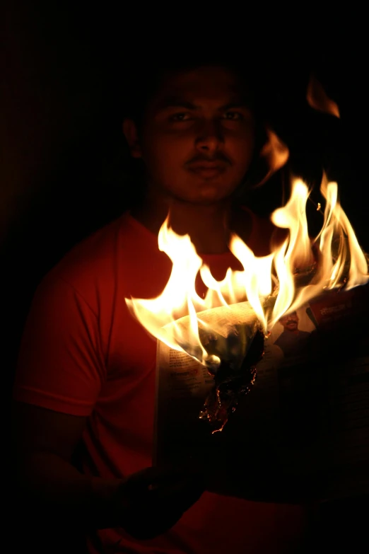 a man in red shirt holding flames while looking at camera