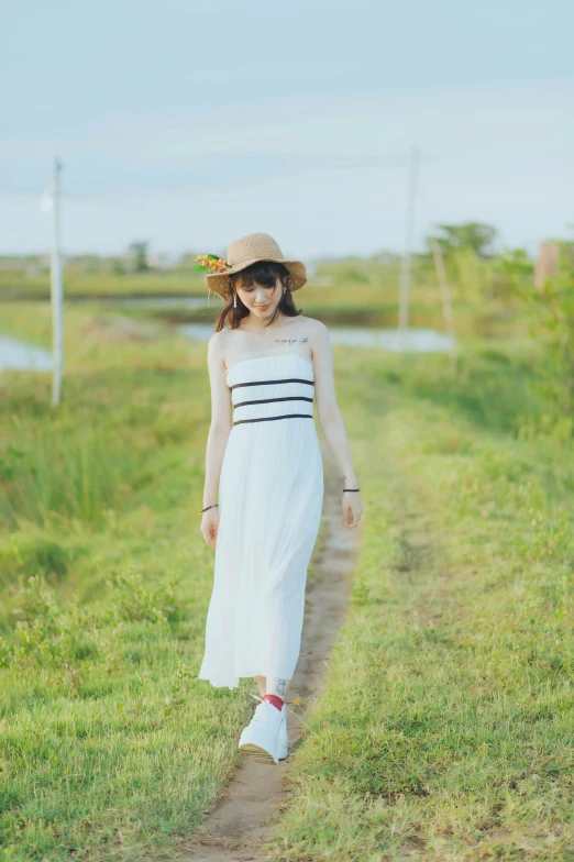 a woman wearing a dress and hat walking on a dirt road