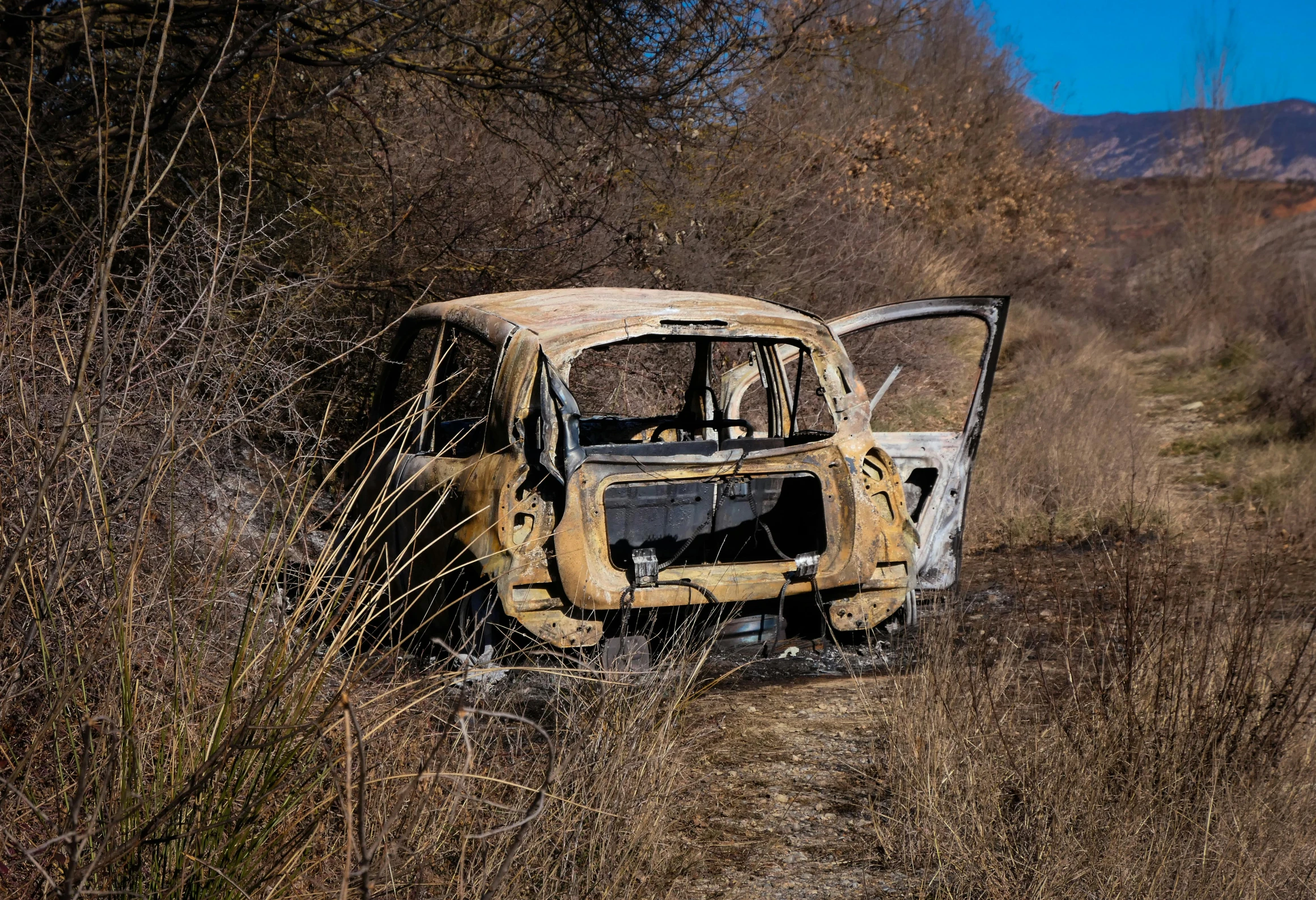 an abandoned, rusty car sitting on a dirt road