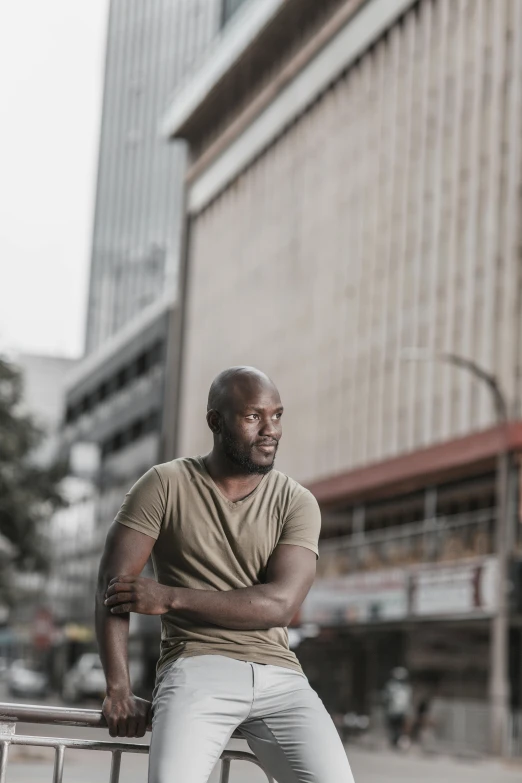 man in brown shirt and jeans leaning against wall with his hands crossed