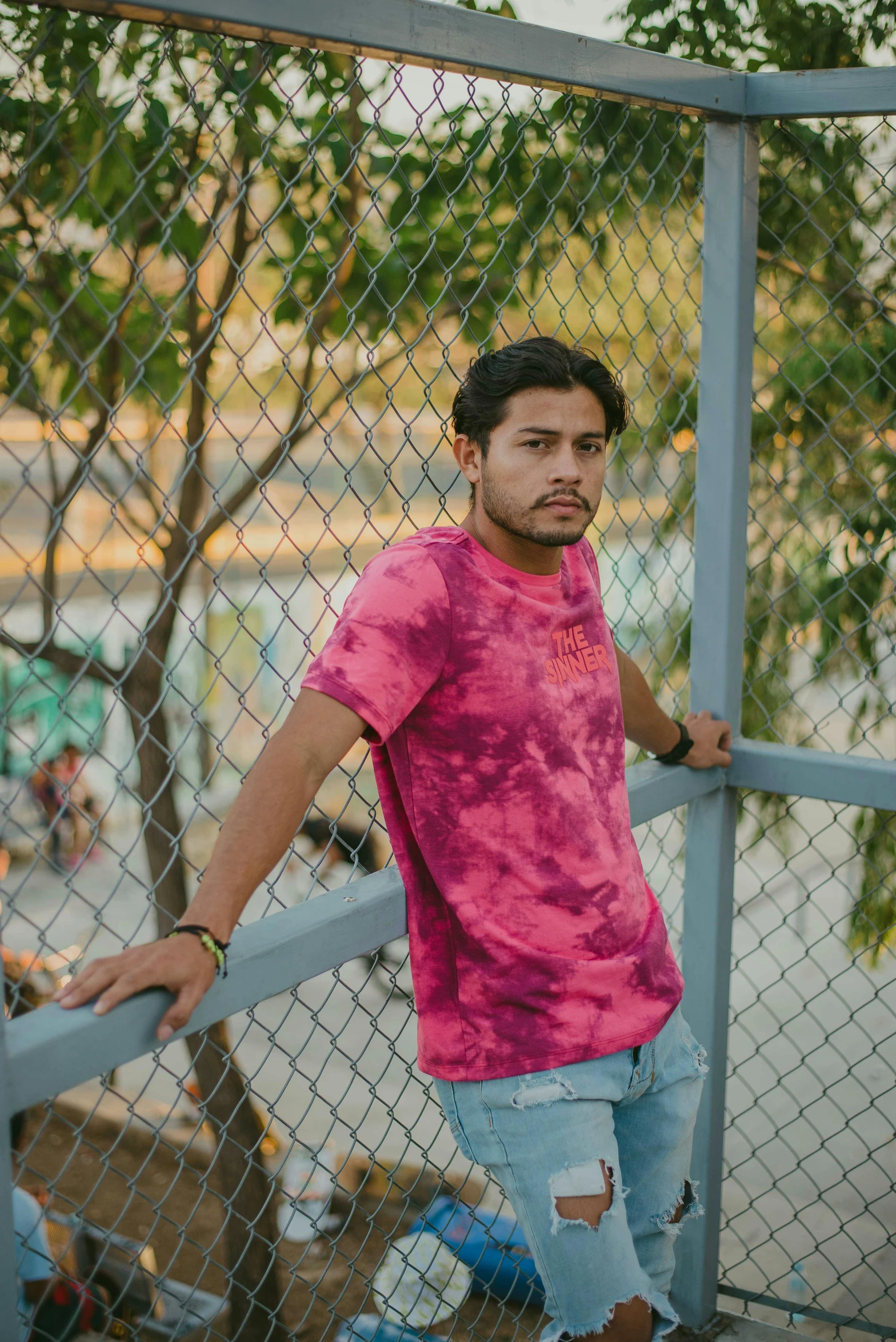 a young man leaning against a fence looking at the camera