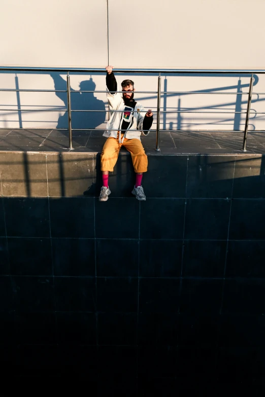 a man in yellow pants and an umbrella sitting on a wall