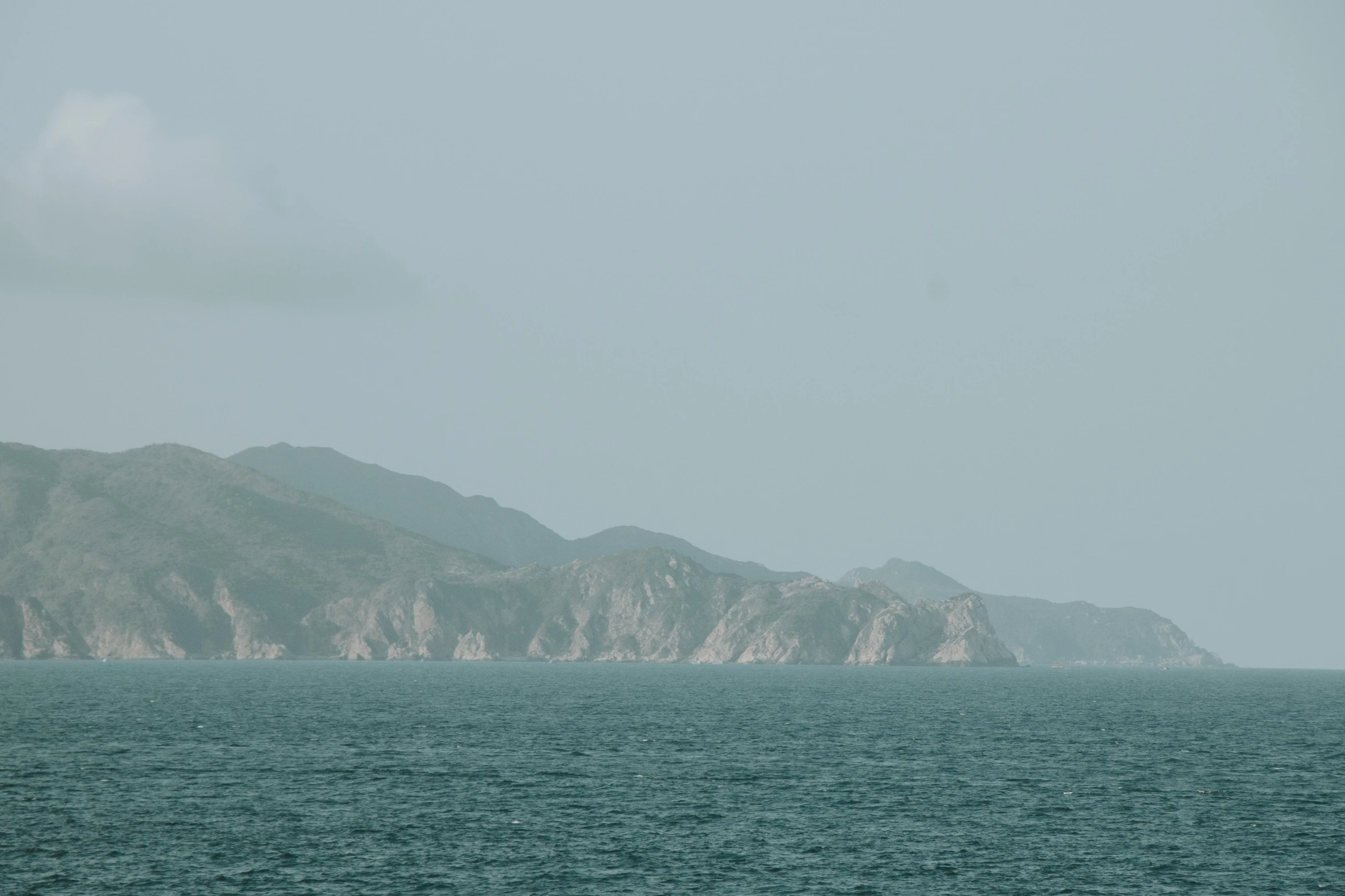 a large hill in the middle of the ocean near mountains