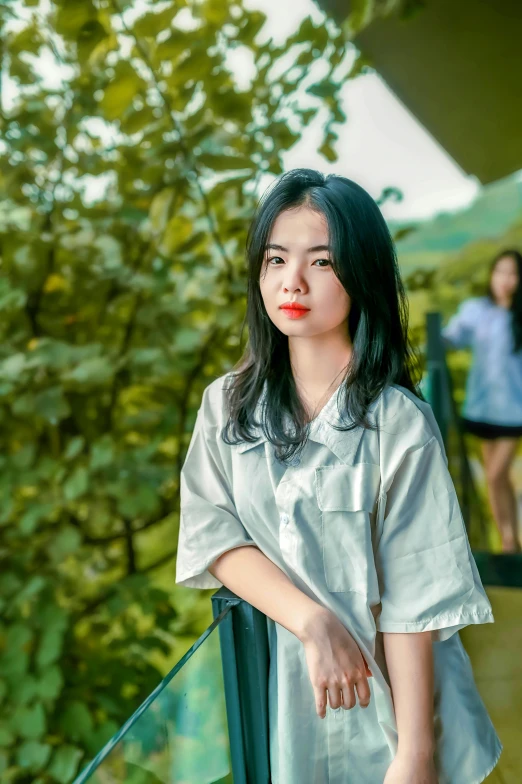 woman in white shirt leaning on rail in front of tree