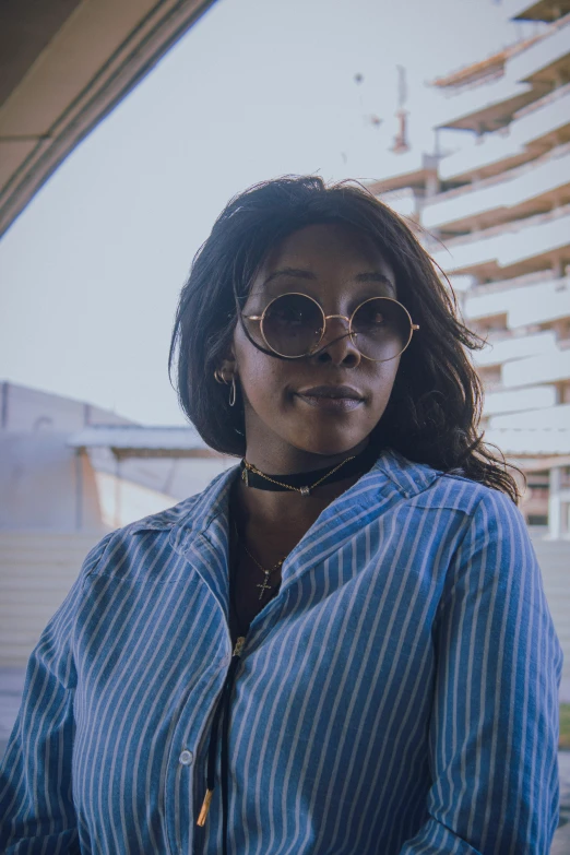 a woman with round glasses stands in front of a building