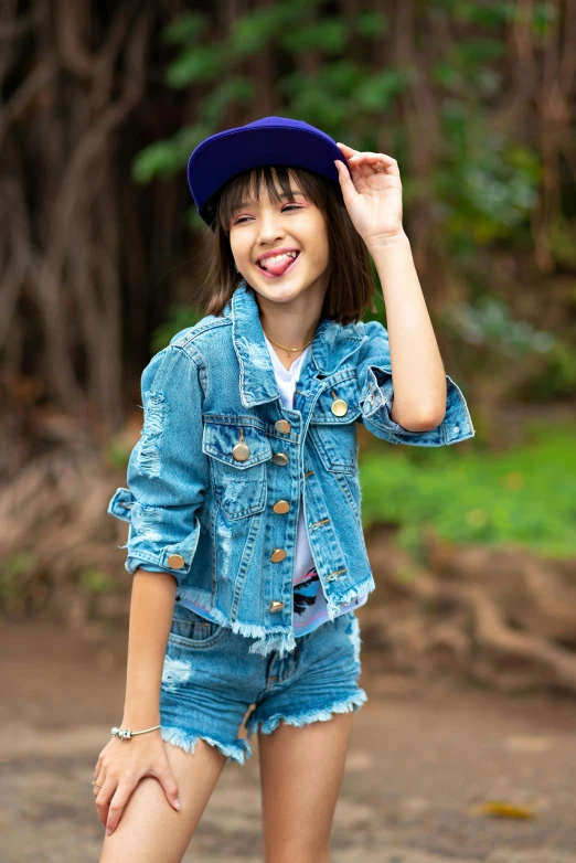 a smiling girl with a blue jean jacket, hat, and denim shorts