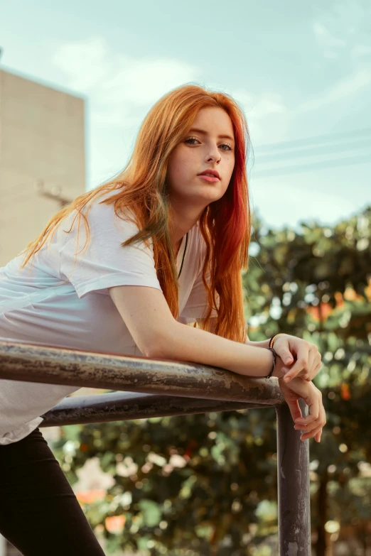 a woman with red hair wearing a white shirt leaning on a metal pole