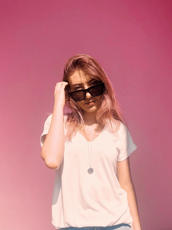 a young woman wearing sunglasses and holding her hair in front of pink walls