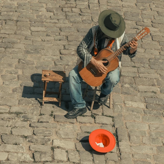 a man sitting on a sidewalk playing a guitar