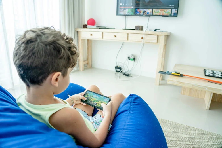 a  in a green shirt sitting on a blue bean bag chair and holding a tablet