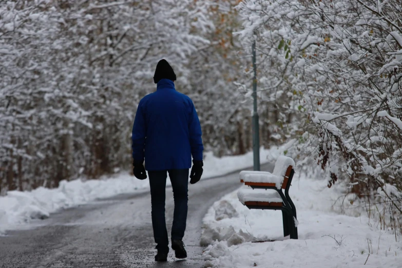 a man walking down a snowy road next to a bench