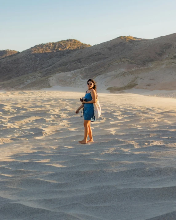 a woman standing on the sand with mountains behind her