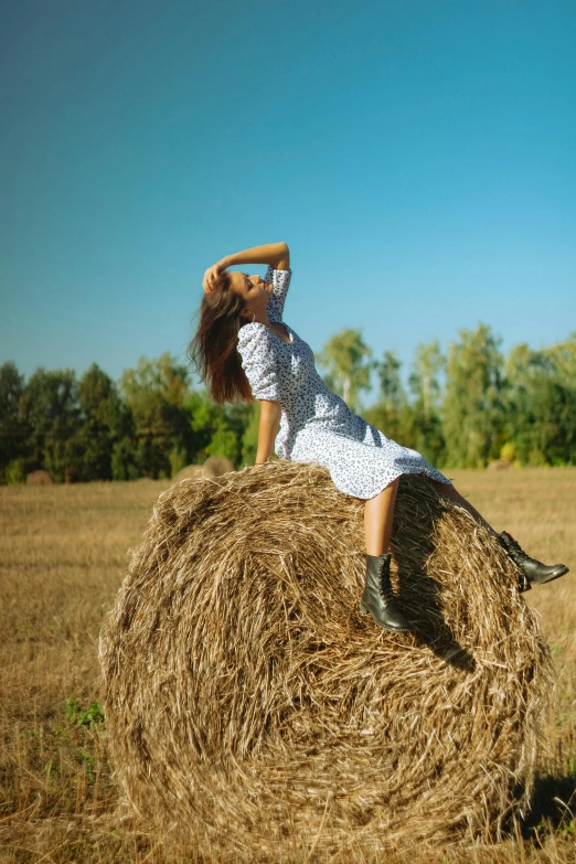 a little girl sitting on a hay bale in a field