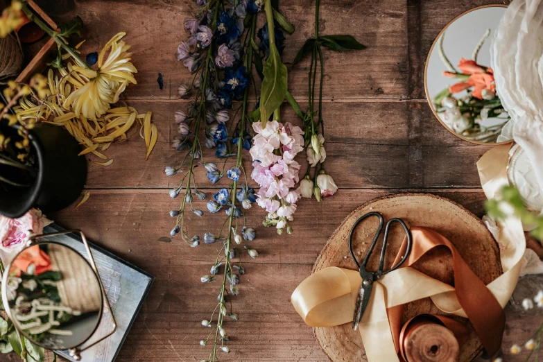 two pairs of scissors and various flowers on a wooden surface