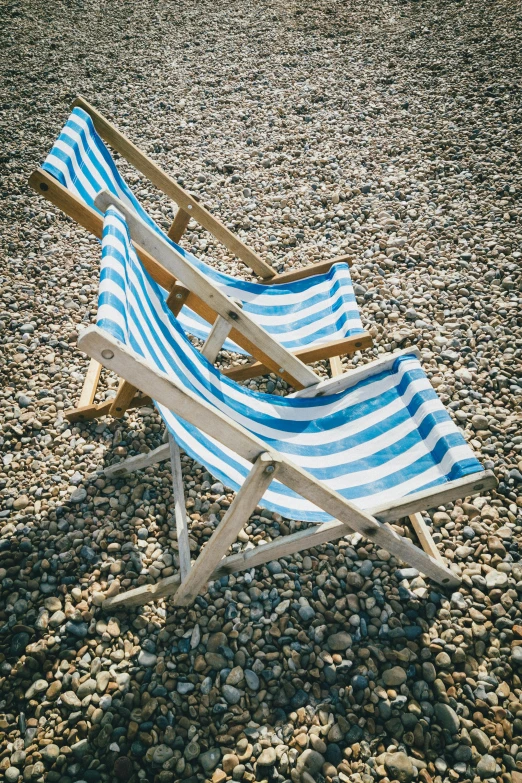 two empty beach chairs sitting on a pebble beach