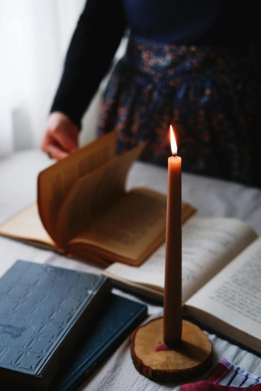 a woman reads an old book next to a lit candle