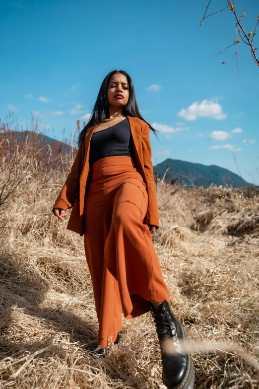 a woman wearing a long skirt and coat walking in a field