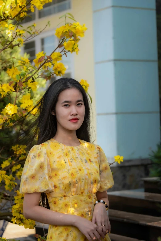 woman standing near yellow flowering tree with building behind