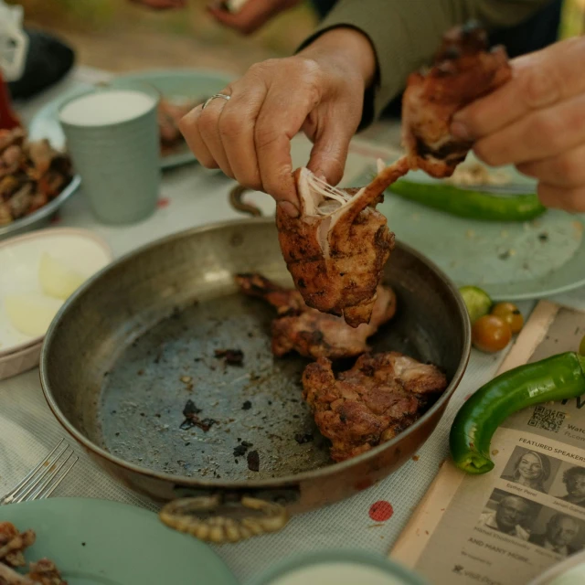 a person dipping some chicken in a pan over other plates