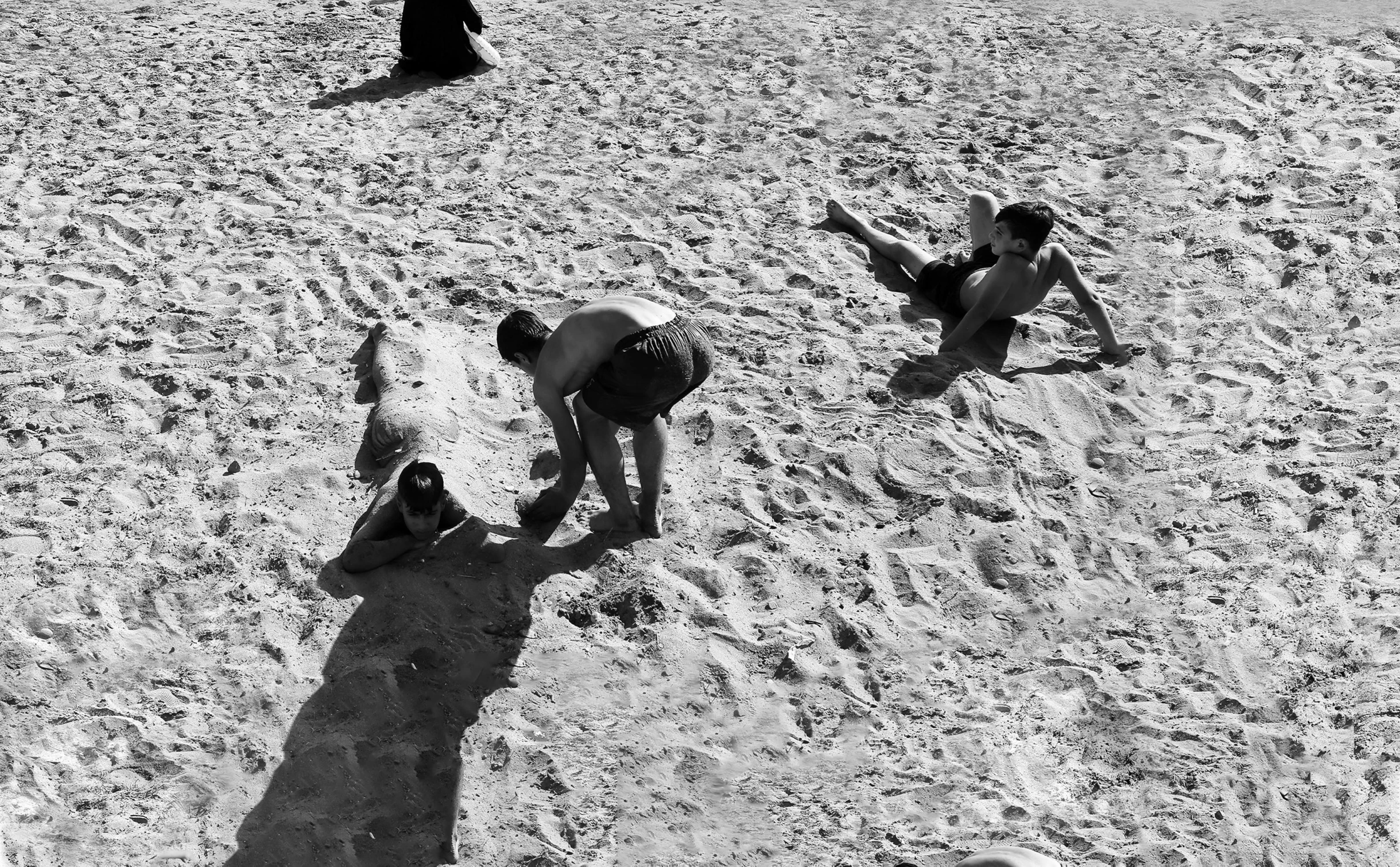 two children play on the beach while a man watches