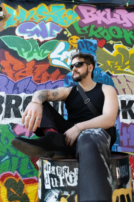 a man in black shirt sitting on wall covered with graffiti